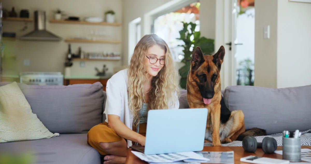 Laptop, typing and dog with woman on sofa for pet insurance research, premium benefits and planner. Animal policy cover, reading and application with person and german shepherd at home for vet claims Dr. Katie Malehorn with a dog